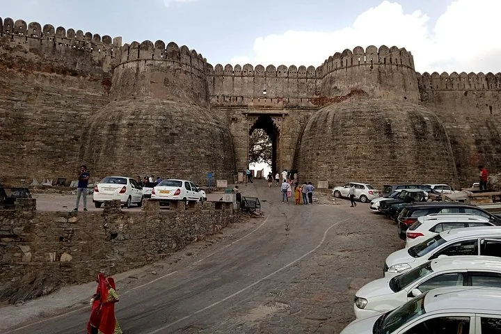 Ein massives Steintor mit geparkten Autos vor der Festung Kumbhalgarh.